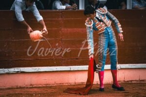 Torero mojando la muleta con agua de un botijo desde el callejón. Detalle traje de luces azul y oro. La preparación - el rito del agua