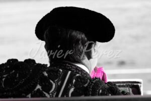 Torero de espaldas con montera esperando en el callejón. Fotografía artística blanco y negro con detalle rosa.