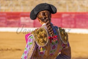 Espalda de torera vestida de lila y oro con trenza natural mirando a la plaza.
